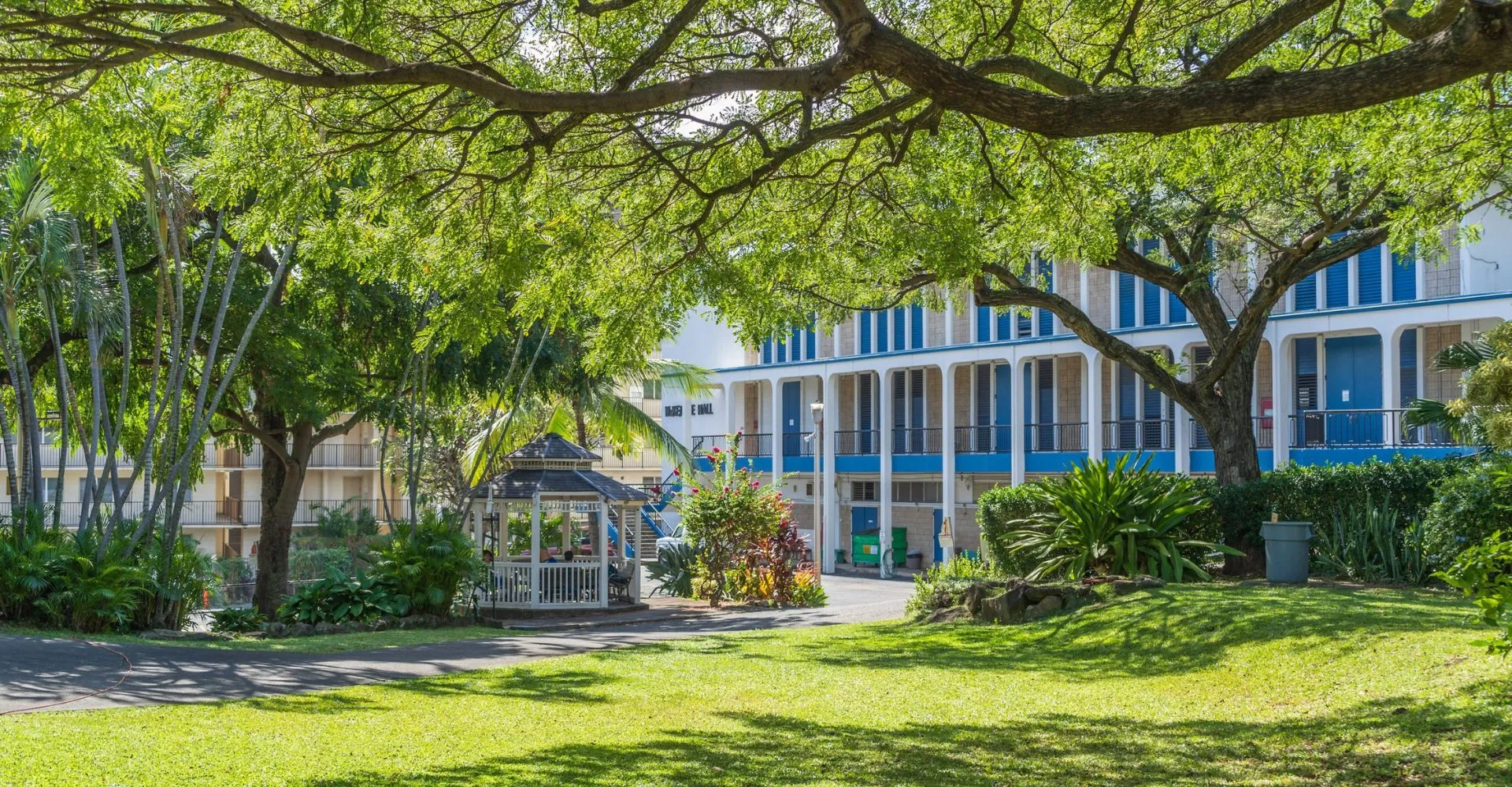 Un giardino verde con gazebo e un edificio bianco e blu all'interno del campus della Hawaiian Mission Academy.