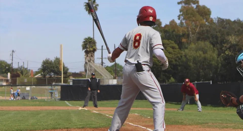 Un giocatore di baseball della Buena High School in maglia bianca con il numero 8 sul campo da gioco con palme sullo sfondo.