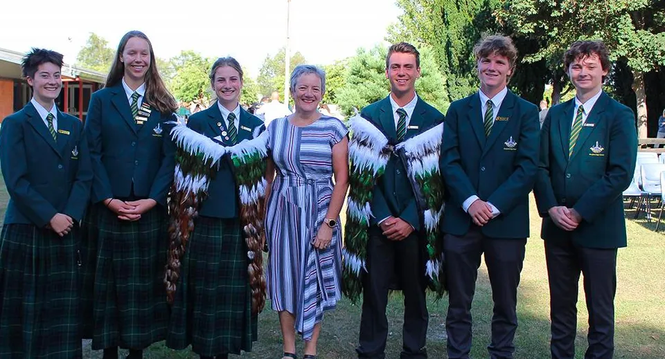 Un gruppo di studenti della Rangiora High School si trova insieme all'aperto davanti ad alberi e spazi verdi.