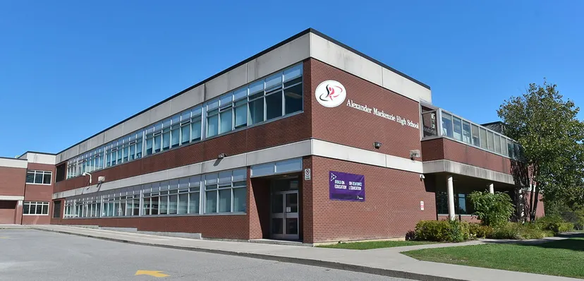 L'edificio in mattoni a più piani della Alexander Mackenzie High School con grandi finestre e il logo sulla facciata sotto un cielo blu.