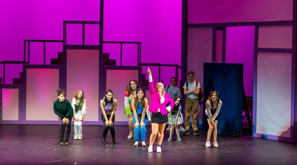 Un gruppo di studenti della Lancaster Country Day School si trova su un palco davanti a uno sfondo multicolore viola e rosa con motivi geometrici.