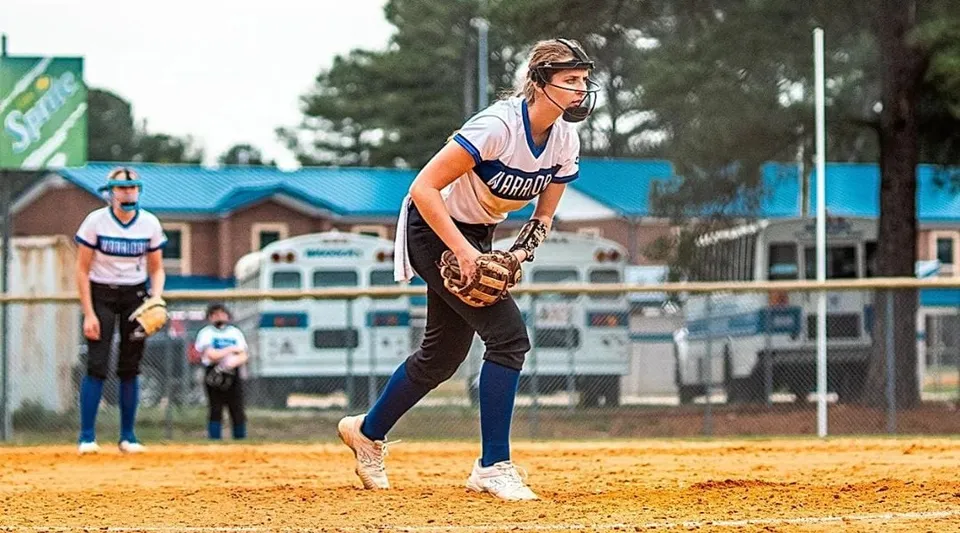 Una studentessa della Fayetteville Christian School si trova sul campo da baseball con diamante e edifici sullo sfondo.
