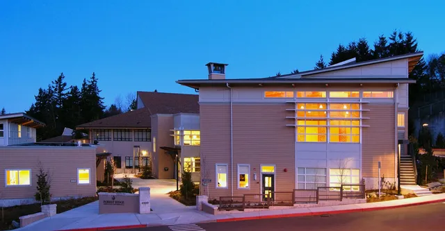 Das mehrstöckige Gebäude der Forest Ridge School of the Sacred Heart steht bei Nacht mit beleuchteten Fenstern umgeben von Bäumen.