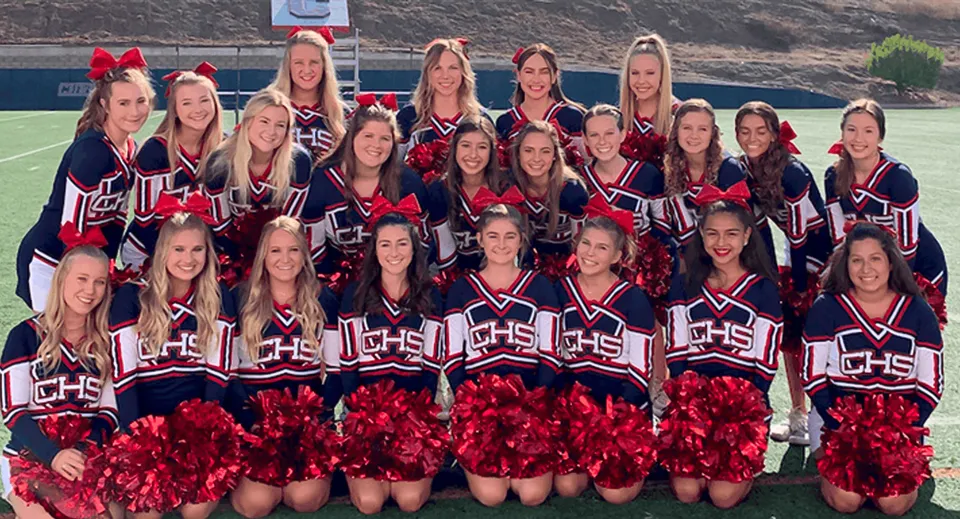Un gruppo di cheerleader posa con divise coordinate e pompon sul campo sportivo delle Christian Unified Schools.