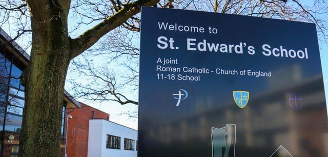 Ein dunkles Schulschild der St. Edward's School neben einem Baum und Schulgebäuden.
