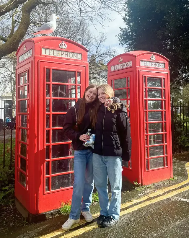Due studentesse abbracciate davanti a due cabine telefoniche rosse britanniche