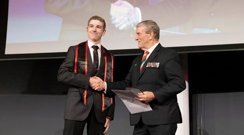 Due uomini in abiti formali si stringono la mano sul palco davanti a uno schermo di proiezione nel campus della Applecross Senior High School.