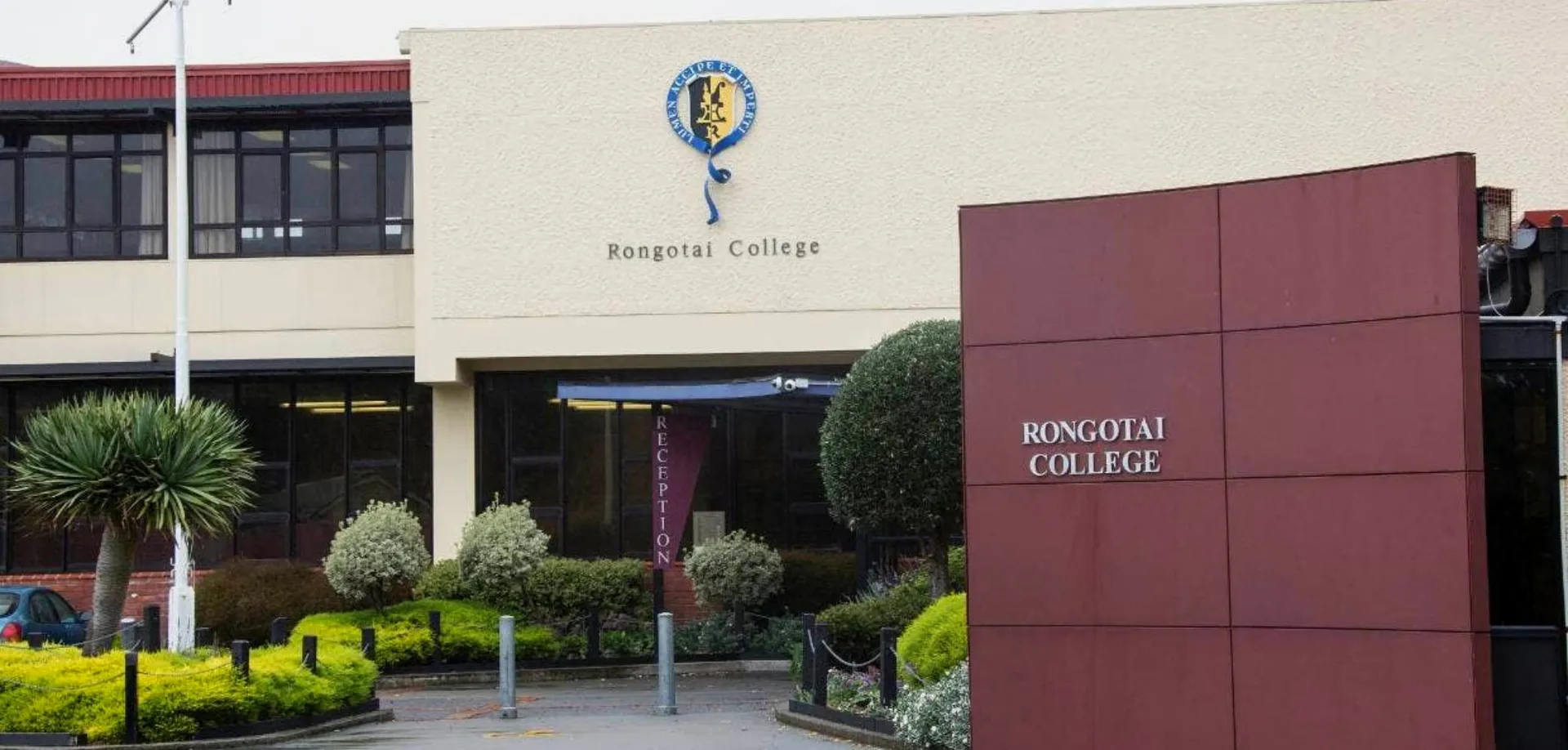 Il moderno edificio in mattoni con la scritta Rongotai College è circondato da una vegetazione ben curata con palme.