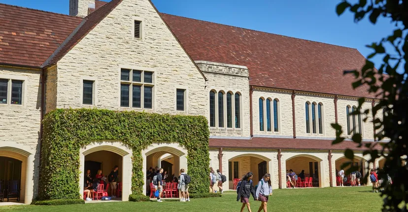 L'ampio edificio in pietra della St. John's School è circondato da un verde lussureggiante e in primo piano ci sono persone sedute sulle panchine.