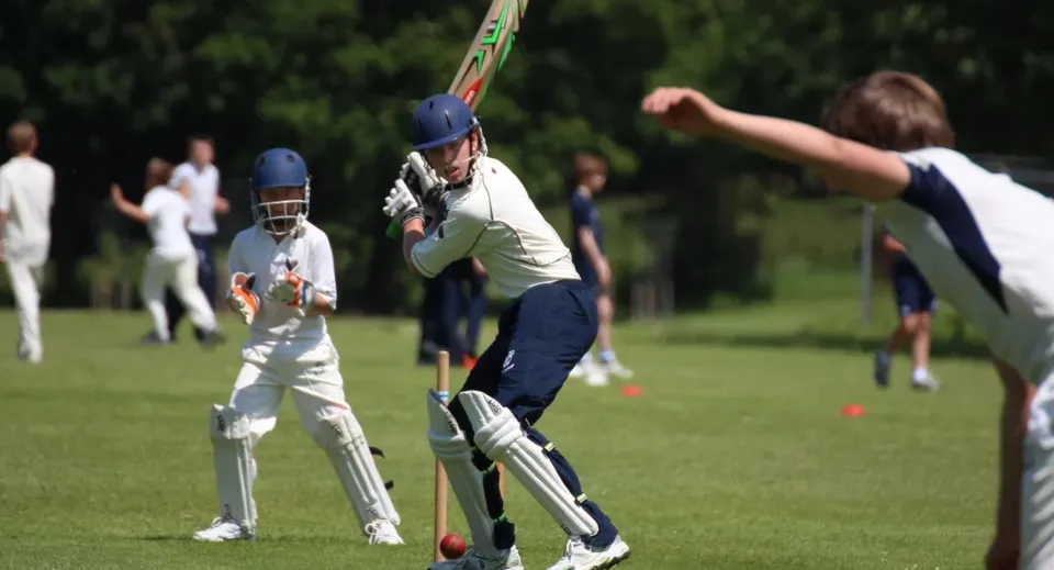 Un giocatore di cricket in maglia bianca mentre colpisce la palla sul campo da gioco del Seaford College.