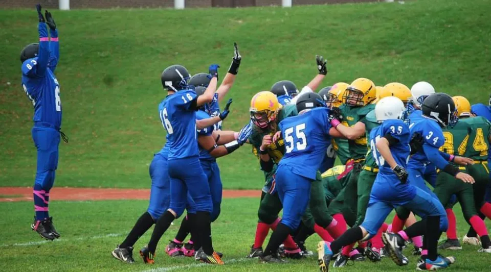 Un gruppo di giocatori di football con maglie blu e gialle gioca sul campo della Aldershot High School.