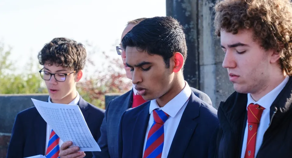 Tre studenti della Loughborough Grammar School discutono insieme con un foglio di carta all'aperto davanti a un edificio scolastico.