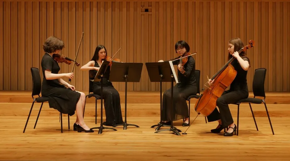 Un quartetto d'archi suona sul palco della Chetham’s School of Music davanti a una parete rivestita in legno.