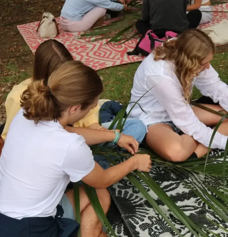 Alumnas sentadas sobre esterillas trenzando hojas de lino en un taller al aire libre