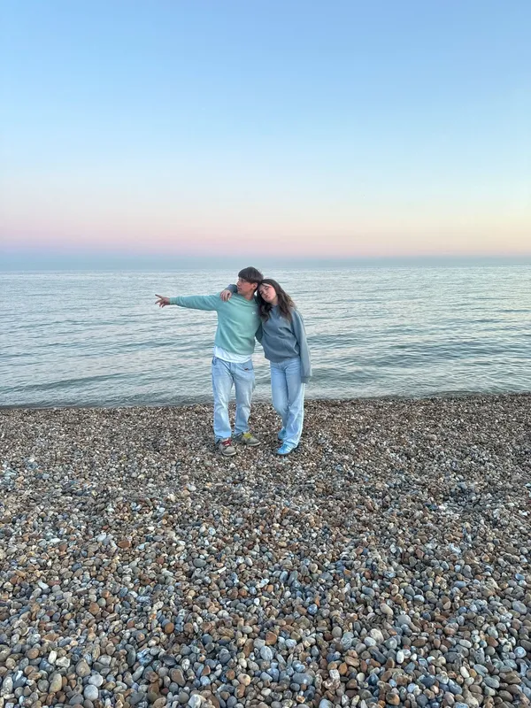 Dos jóvenes abrazados en una playa de guijarros con el mar en calma al atardecer