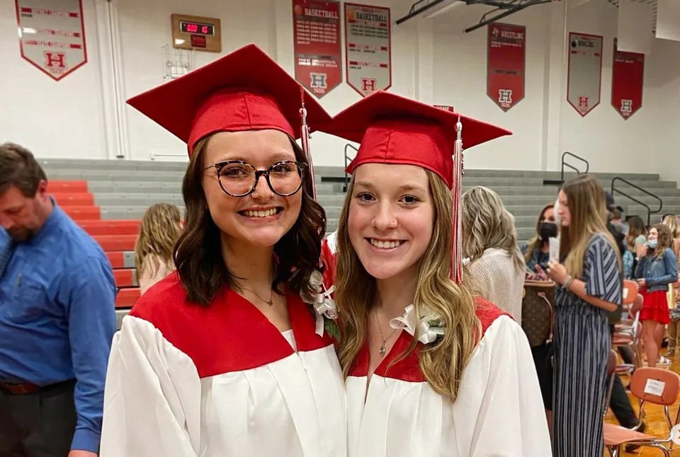 Due studentesse indossano tocchi e toghe rossi e posano alla Huron High School vicino alle decorazioni per la cerimonia di diploma.