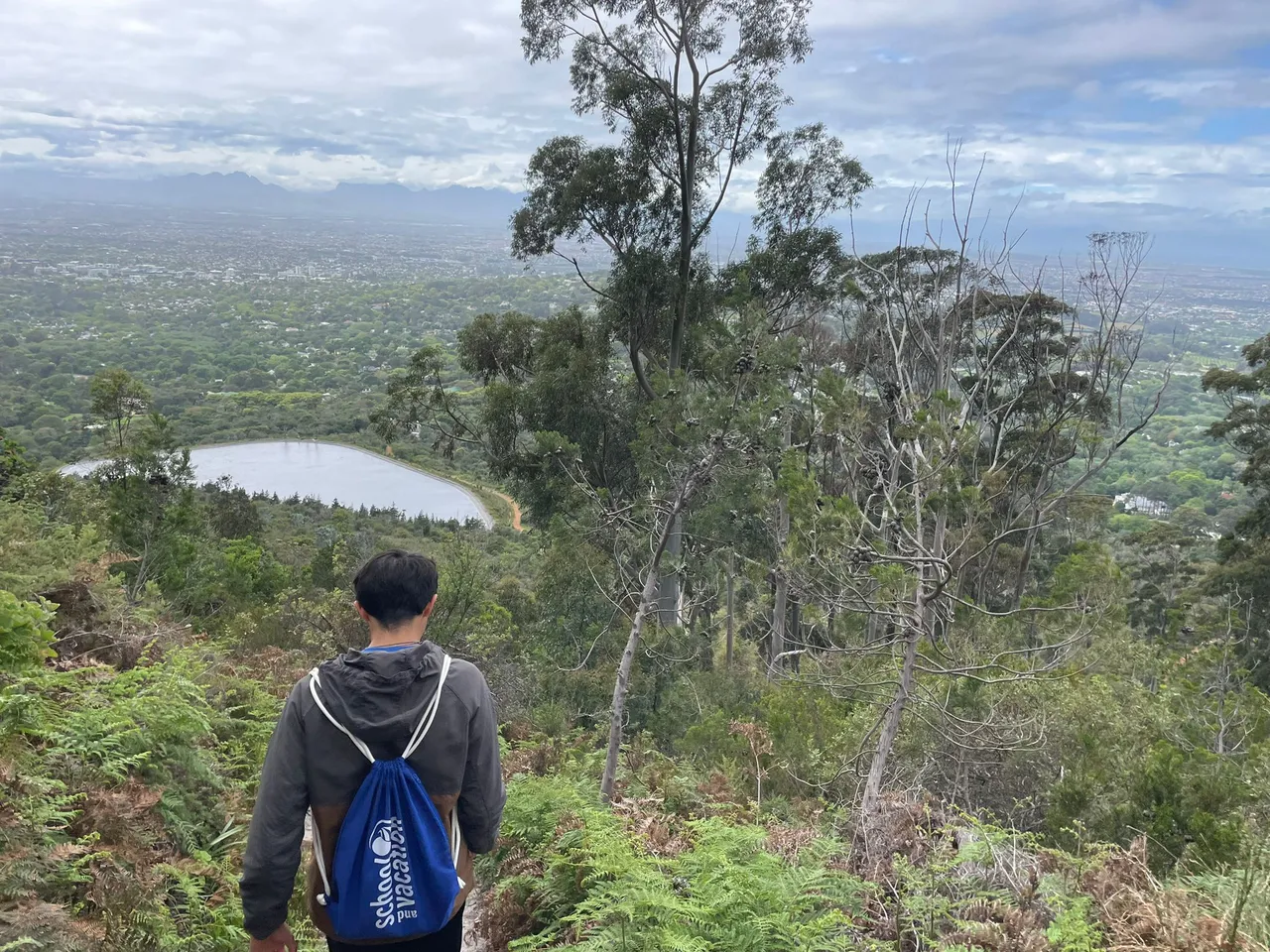 Studente con zaino School and Vacation su un sentiero panoramico sopra una città in Sudafrica
