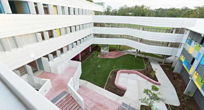Si vede il moderno edificio a più piani della Indooroopilly State High School con un cortile interno e percorsi rosa.