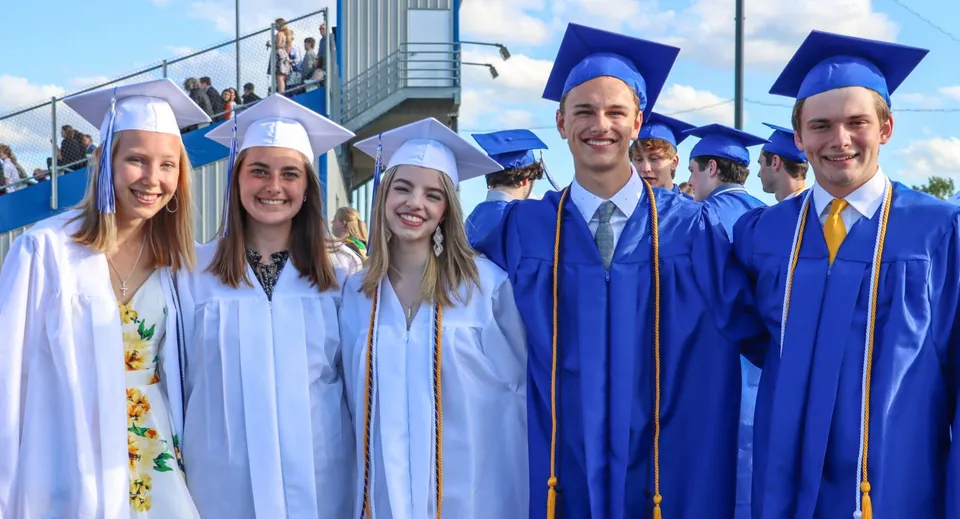 Un gruppo di diplomati della St. Mary Catholic High School in abiti blu davanti a un edificio scolastico.