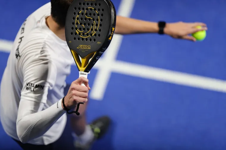 Padelspieler in weißem Shirt holt mit Schläger und Ball zum Aufschlag aus