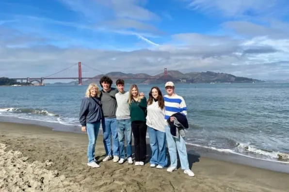 Grupo de jóvenes posando en una playa con un gran puente rojo de fondo