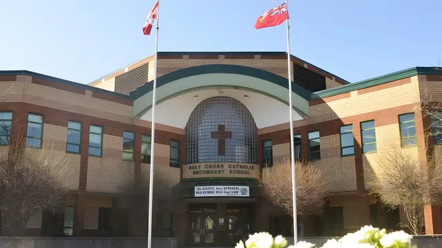 Das Gebäude der Holy Cross Catholic Secondary School mit den kanadischen und chinesischen Flaggen vor blauem Himmel und Bäumen.