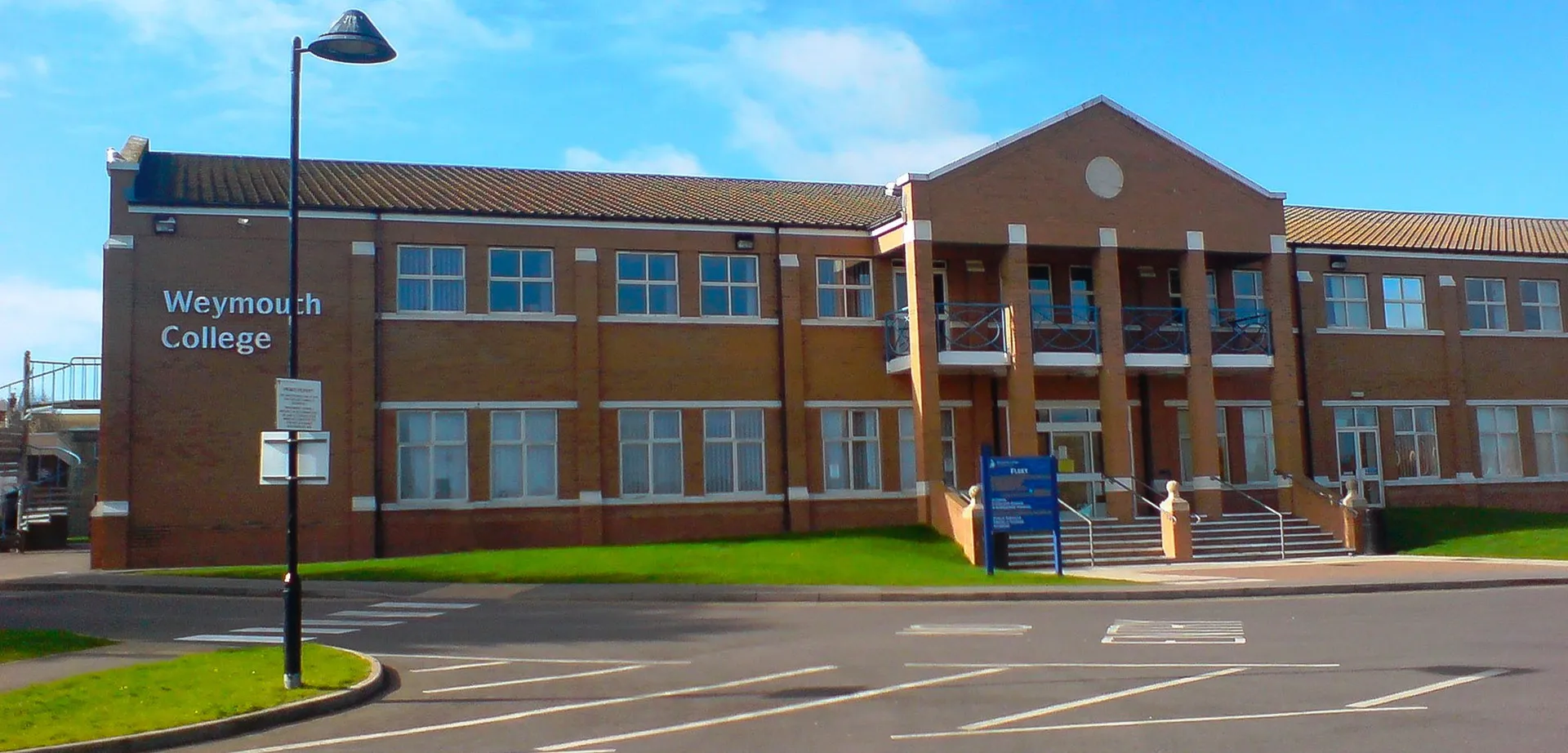 L'edificio in mattoni a più piani con ampie finestre del Weymouth College è circondato da un parcheggio pavimentato e da aree verdi.