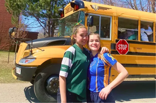 Dos estudiantes junto a un autobús escolar amarillo en Canadá