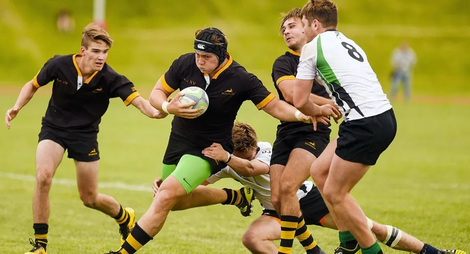 Studenti della All Saints Anglican School giocano un'intensa partita di rugby su un campo verde.