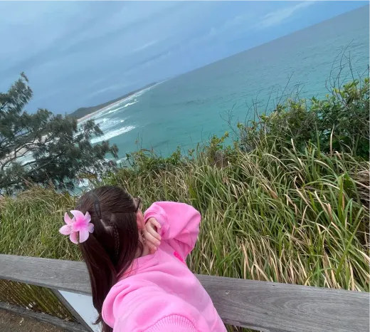 Antonia blickt in rosa Pullover von einem Aussichtspunkt auf Ozean und Küste in Australien