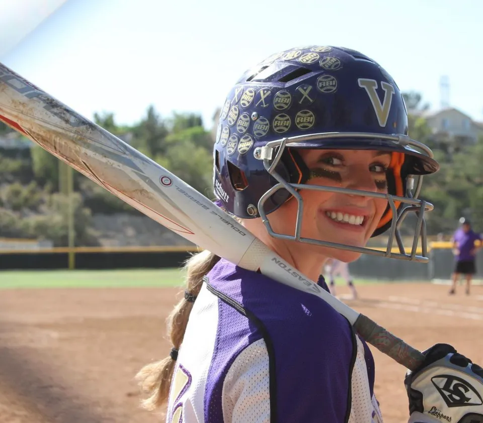 Una giovane giocatrice di softball si trova sul campo da baseball della Valencia High School con un bosco sullo sfondo.