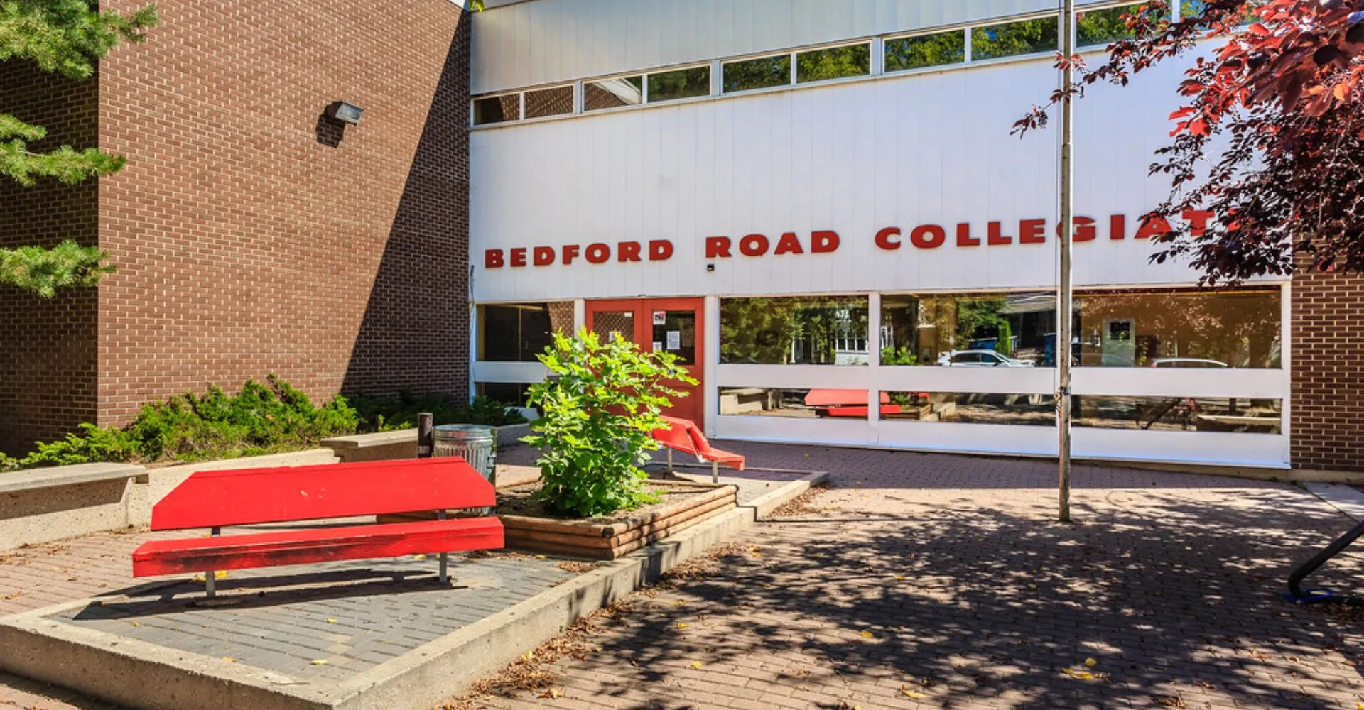 L'edificio in mattoni del Bedford Road Collegiate con grandi finestre è circondato da alberi e panchine.