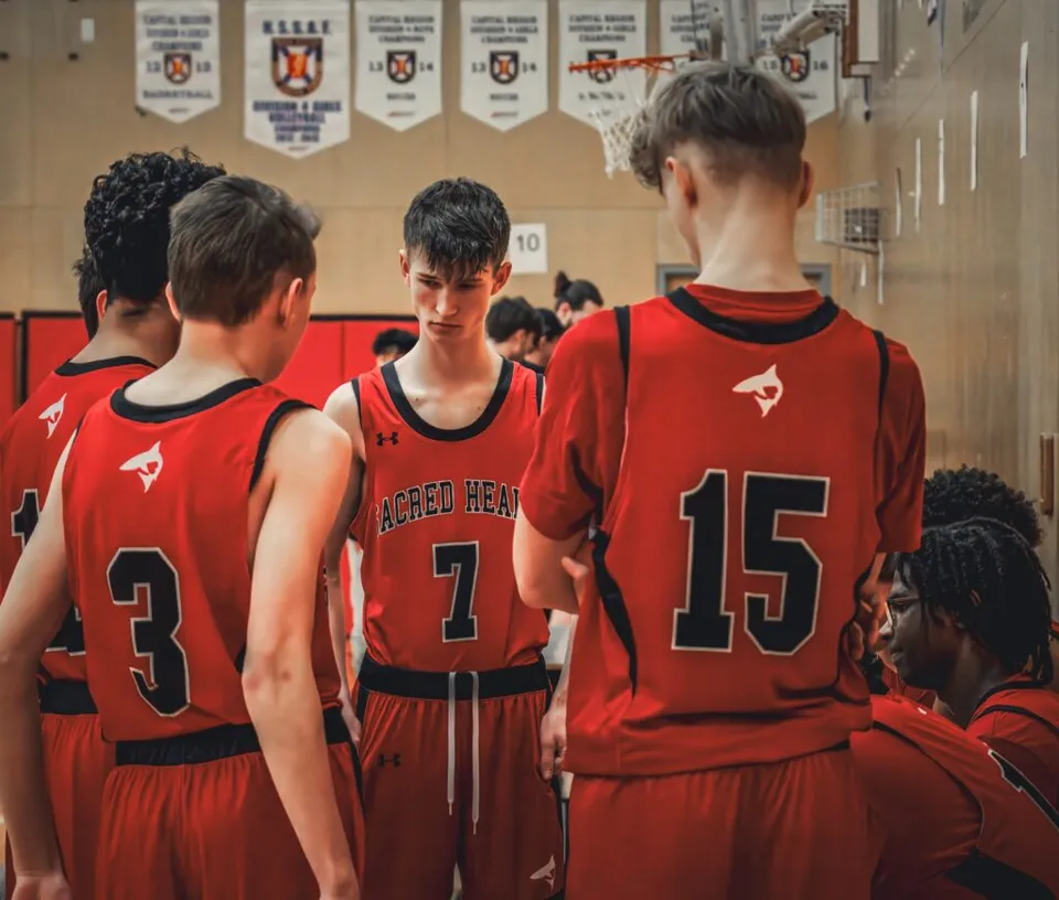 Studenti della Sacred Heart School of Halifax indossano maglie rosse e stanno insieme nello spogliatoio della squadra di basket.