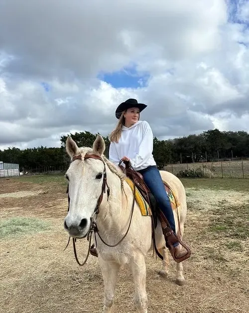Ragazza con cappello da cowboy cavalca un cavallo bianco in un ranch