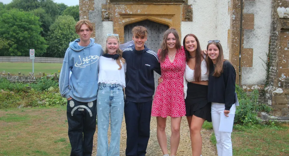 Sei giovani studenti sorridono in piedi davanti a un edificio in pietra della Leweston School.