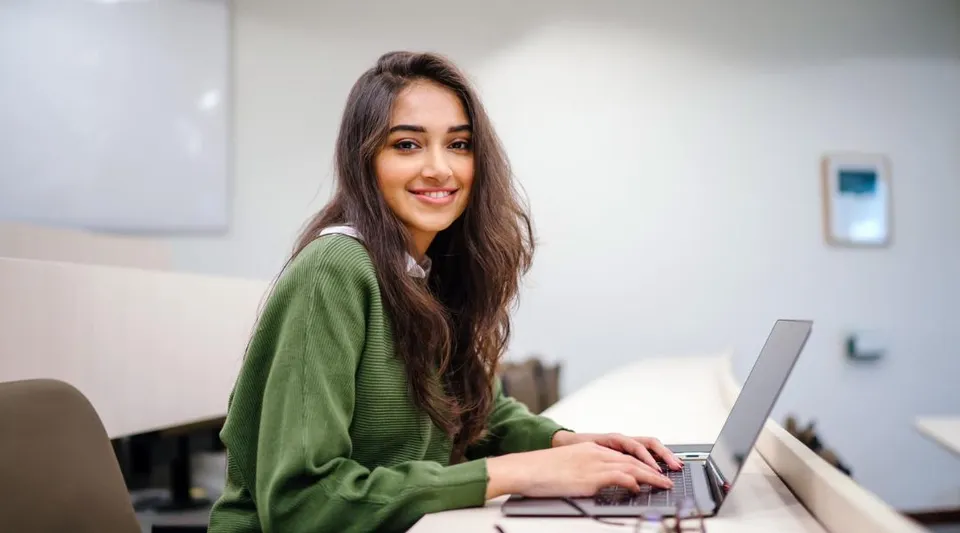 Una giovane donna è seduta a una scrivania e usa un laptop nell'area di lavoro del David Game College Liverpool.