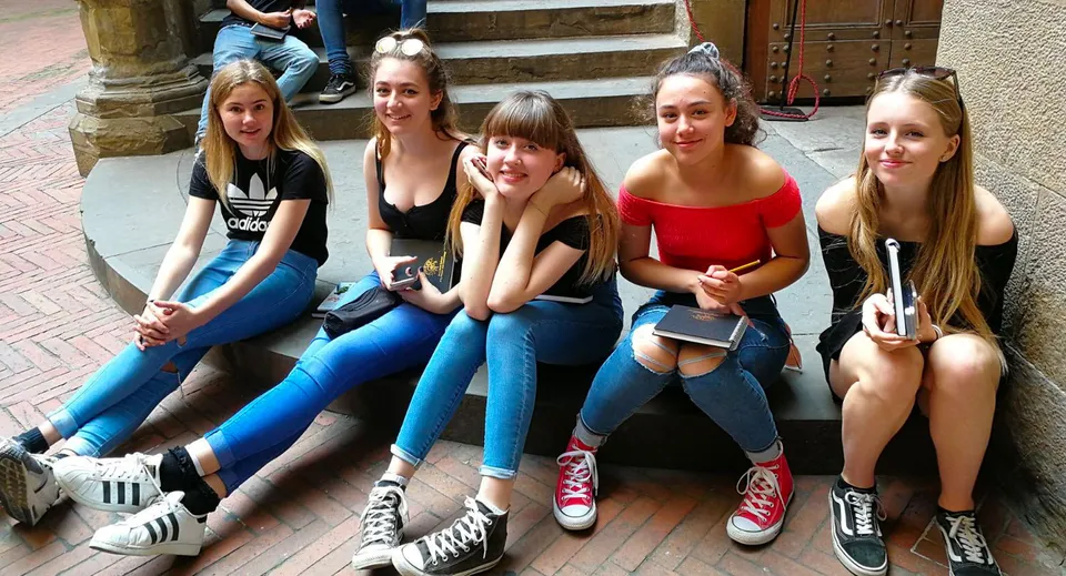 Un gruppo di studentesse è seduto sui gradini di un edificio nel campus della Denefield School e chiacchiera.