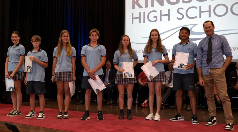 Un gruppo di studenti e studentesse si trova sul palco della Kingscliff High School con in mano certificati o premi.