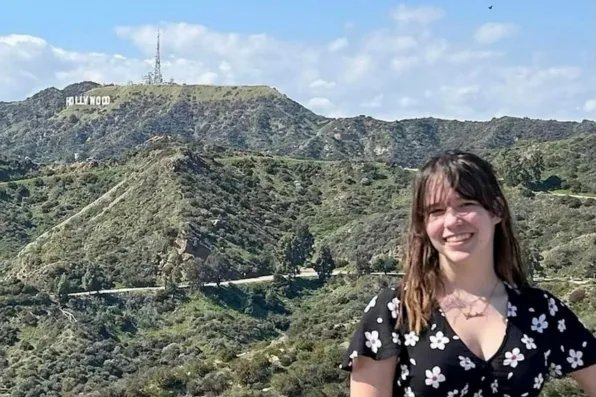 Chica sonriente con vestido floral y colinas al fondo con el cartel de Hollywood