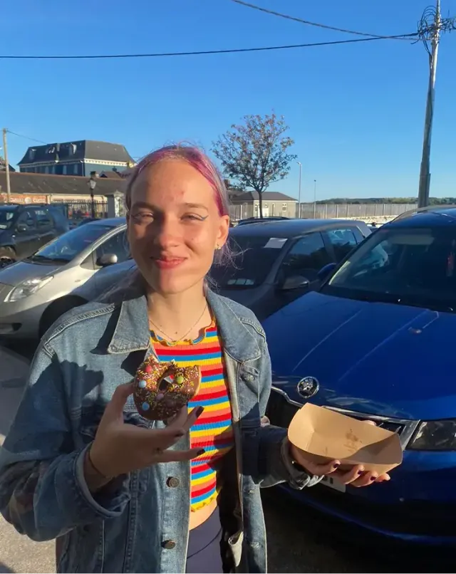 Ragazza sorridente tiene una ciambella al cioccolato in un parcheggio