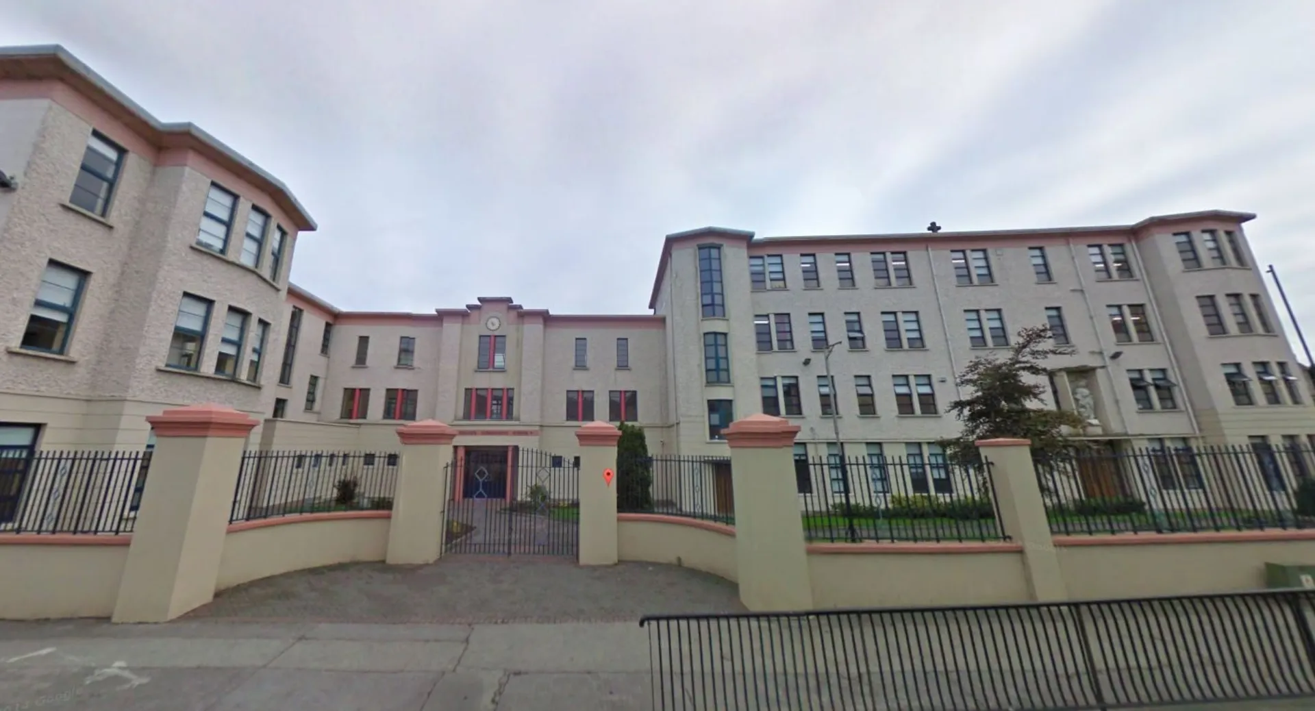 L'edificio a più piani in mattoni e pietra arenaria della Mountmellick Community School, con elaborati dettagli architettonici, è circondato da una recinzione metallica.