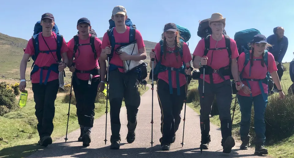 Un gruppo di studenti della Bryanston School indossa un abbigliamento da trekking rosa coordinato in un ambiente paesaggistico suggestivo con montagne sullo sfondo.
