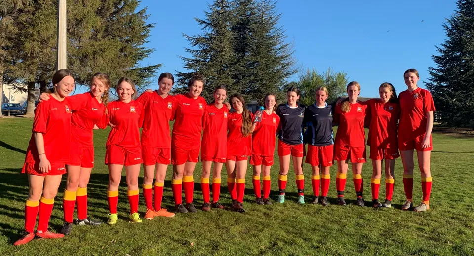 Un gruppo di giovani calciatrici in maglia rossa si trova su un campo sportivo della Dunstan High School.