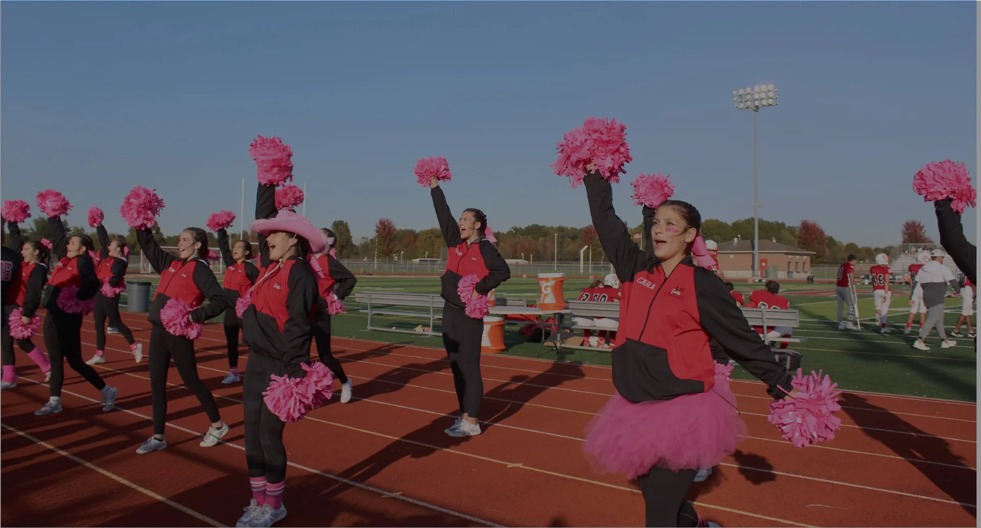Cheerleaderinnen in pink-schwarzen Uniformen jubeln mit Pompons am Spielfeldrand