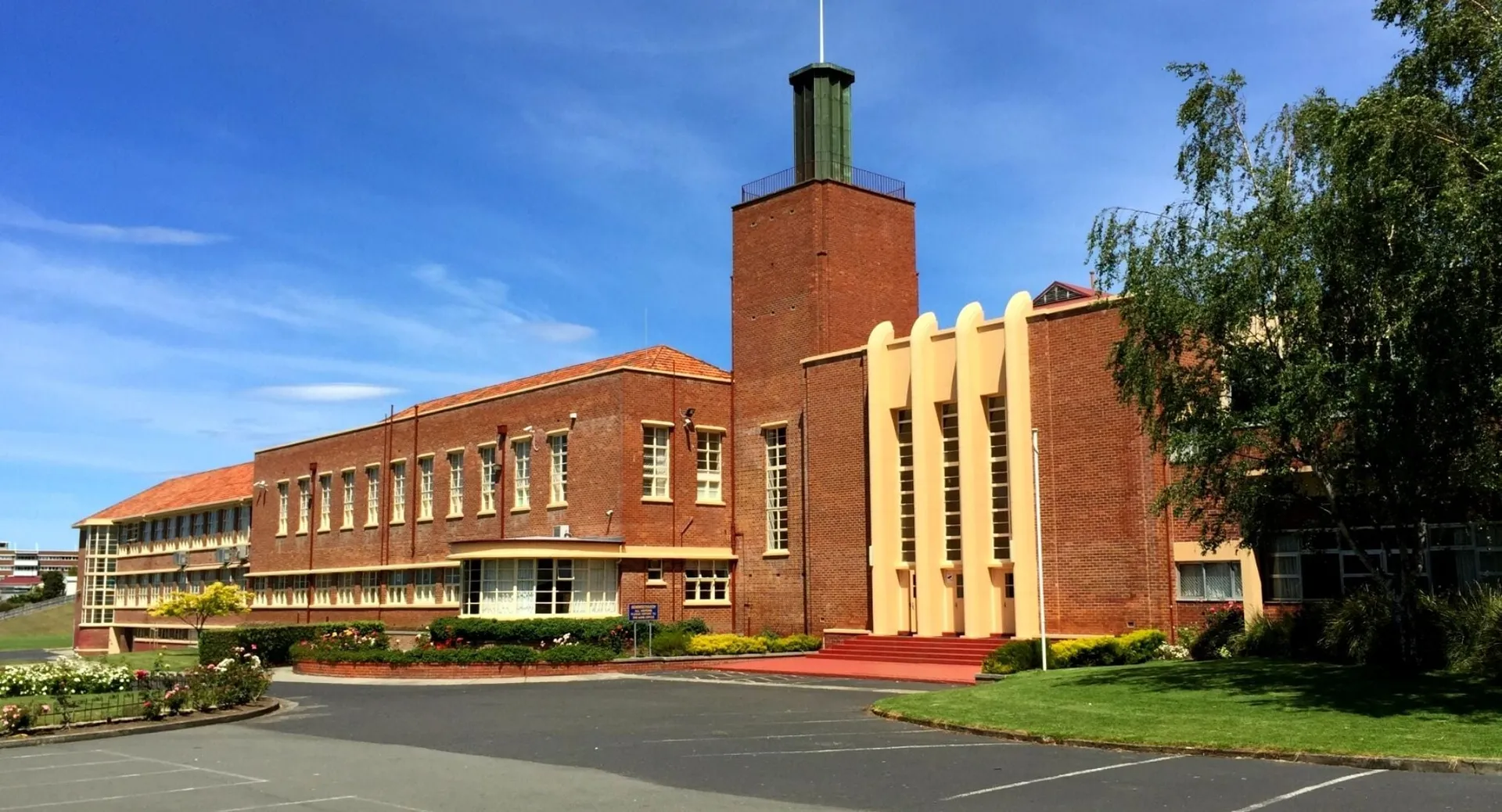 L'ampio edificio in mattoni con un alto comignolo nel campus della Hobart City High School è circondato da alberi e da un vialetto d'accesso.