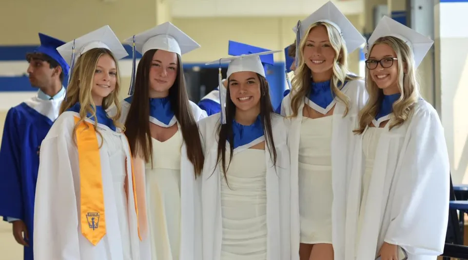 Un gruppo di studentesse della Conwell-Egan Catholic High School è in piedi insieme con abiti e tocchi bianchi da diploma e posa per una foto.