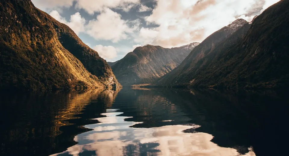 Si vede un fiordo tranquillo con una superficie dell'acqua riflettente e alte montagne sullo sfondo.