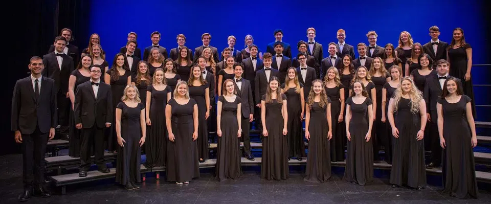 Un gruppo di studenti e studentesse della Holy Heart of Mary High School in abiti eleganti su un palco con uno sfondo blu.