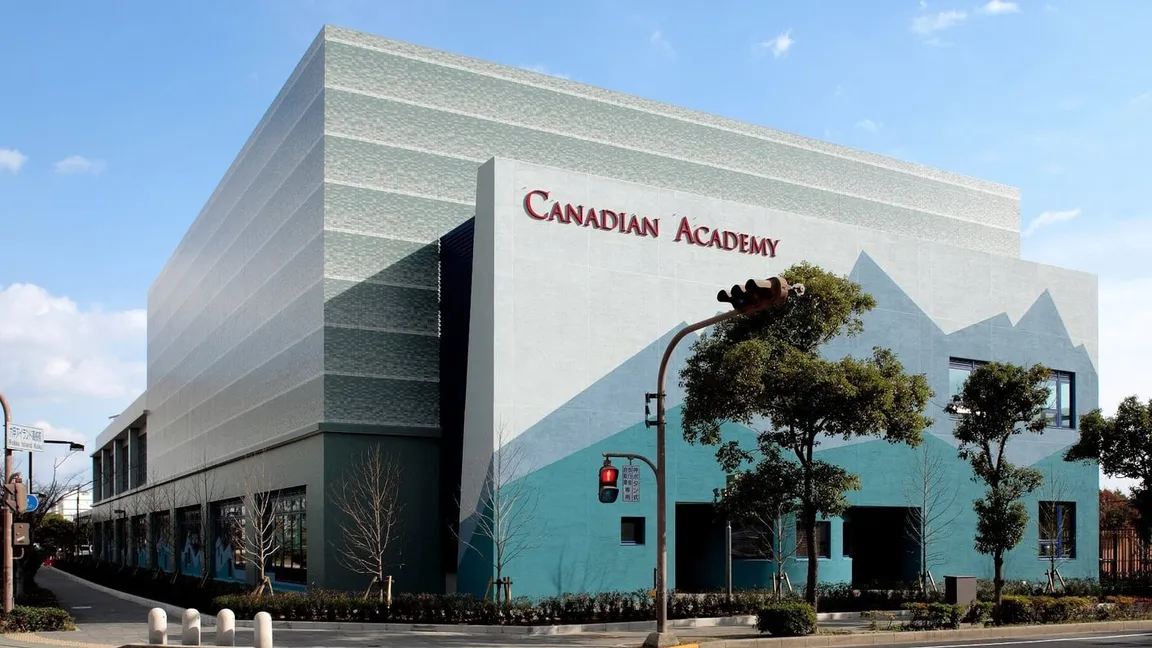 Mehrstöckiges Schulgebäude mit bemalter Fassade und Schriftzug Canadian Academy an einer Straßenkreuzung