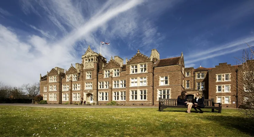 L'edificio principale storico della Monmouth School for Girls sorge su un prato verde sotto un cielo azzurro con nuvole.